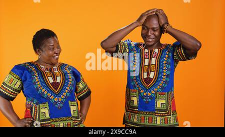 Fröhlicher Mann und Frau, die zusammen im Studio lachen, Spaß mit dummen Witzen über orangem Hintergrund haben. afroamerikaner genießen lustige Momente mit Lachen, amüsantes Paar. Stockfoto