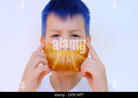 Nahaufnahme des Gesichts des Kindes, Junge von 8 Jahren hält rosige gebackene Croissants mit Händen nahe dem Mund, zeigt fröhliches Lächeln, Konzept köstliches Frühstück, ha Stockfoto