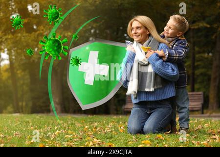 Glückliche Mutter mit ihrem Sohn auf grünem Gras im Herbstpark. Starke Immunität - Schutz gegen Viren Stockfoto