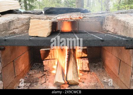 Eine Nahansicht eines gemauerten Außenkampfes mit einem Metallgitter, darunter brennenden Holzstämmen und einem Grillkorb oben. Stockfoto