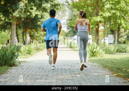 Mann und Frau, die an einem sonnigen Tag gemeinsam auf einem Parkweg joggen, beide tragen Sportkleidung Stockfoto