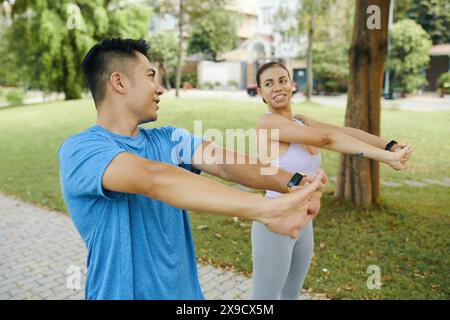 Mann und Frau in sportlicher Kleidung wärmen sich zusammen, indem sie ihre Arme während einer Outdoor-Übung im Park Strecken Stockfoto