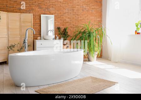 Das stilvolle Badezimmer verfügt über Waschbecken, Kommode, Spiegel, Badewanne und Zimmerpflanze Stockfoto