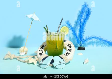 Glas leckerer Cocktail mit Rettungsschirm, Muscheln, Regenschirm und Flipflops auf blauem Hintergrund Stockfoto