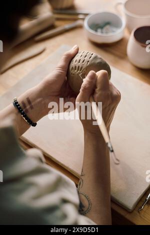 Vertikaler Hochwinkelschuss von Händen nicht erkennbarer Handwerker mit Tonschnitzerei-Werkzeug zur Dekoration handgefertigter Keramikschale Stockfoto