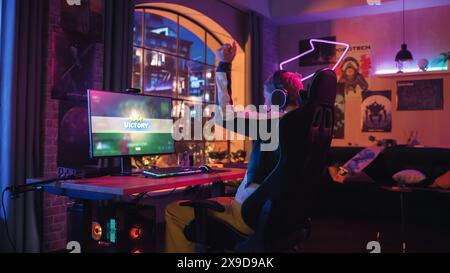 Erfolgreiche weibliche Gamer spielen und gewinnen im 3D-Shooter-Videospiel, in dem die Spieler in einem Turnier auf dem PC kämpfen. Stilvolle junge Frau feiert den Sieg in einem gemütlichen Zimmer zu Hause. Stockfoto