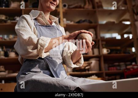 Sonnendurchflutete Aufnahme einer kreativen Seniorin, die eine Tonkugel in der Hand hält und im Kopierraum des Kunststudios Töpferunterricht genießt Stockfoto