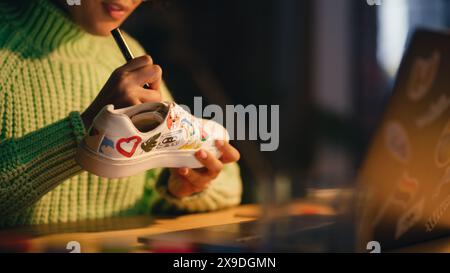 Nahaufnahme von Black Female Designerin, die ihre einzigartige Zeichnung auf Schuhen platziert hat und spät am Abend im Loft Living Room arbeitet. Millennial People und Modetrends im Bekleidungsdesign-Konzept. Stockfoto