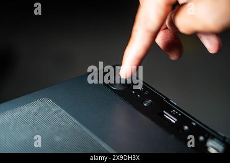 Nahaufnahme einer Person, die den ein-/Ausschalter an einem Desktop-Computer-Gehäuse drückt. Das Bild fokussiert sich auf das obere Bedienfeld des Computergehäuses und zeigt t Stockfoto