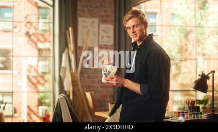 Konzentrierter männlicher Künstler, der im Loft Studio an dem bunten Bold Design von Sneakers arbeitet. Modedesigner personalisiert ein Paar Schuhe mit seiner eigenen Kunst und schaut in die Kamera. Kreative Der Neuen Generation. Stockfoto