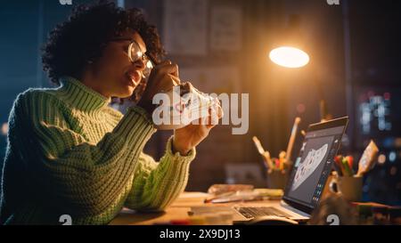 Millennial Designer Workspace: Brasilianische Künstlerin sitzt am Schreibtisch und wendet ihre eigenen Designs auf den Custom Schuh an. Frau, die spät am Abend arbeitet. Menschen mit einem einzigartigen Ideenkonzept. Stockfoto