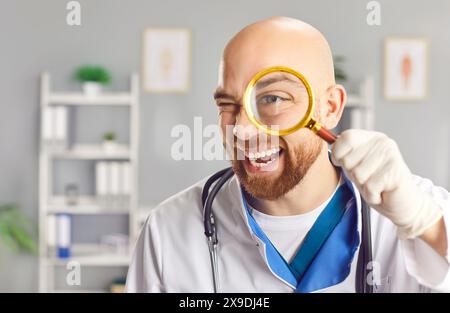 Der fröhliche Arzt wird gesehen, wie er breit zuzwinkert und lächelt, während er die Lupe an sein Auge hält. Stockfoto