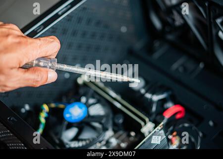 Eine Person, die einen Applikator für Wärmeleitpaste über einem offenen Computergehäuse mit sichtbaren Komponenten wie dem CPU-Kühler und der Grafikkarte hält. Stockfoto