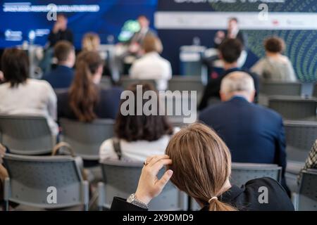 Eine Gruppe von Geschäftsleuten, die an einer Konferenz teilnehmen und einem Sprecher auf der Bühne aufmerksam zuhören. Der Fokus liegt auf der Rückseite des Publikums. Stockfoto