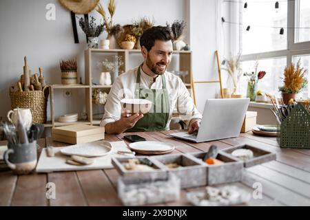 Erwachsener Besitzer eines Keramikgeschäfts mit Laptop während der Arbeit im Geschäft. Stockfoto