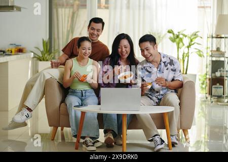 Vier Freunde versammelten sich auf einer Couch, genossen Snacks und sahen sich gemeinsam einen Film an, in einem gemütlichen und einladenden Wohnzimmer Stockfoto