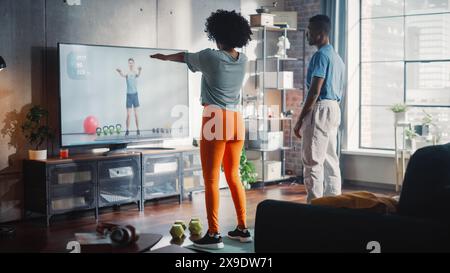 Black Strong Pärchen trainiert gemeinsam zu Hause und sieht sich das Tutorial im Fernsehen an. Wunderschöner Freund und Freundin in Sportkleidung machen Fitness-Übungen. Erfolgreiches Körperliches Training. Stockfoto