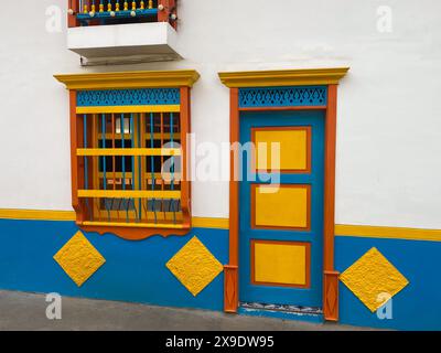 Eine lebhafte Kolonialfassade mit dekorativem Fenster und Tür in Blau, Gelb und Orange, die traditionelle architektonische Elemente und Farbtöne hervorheben Stockfoto