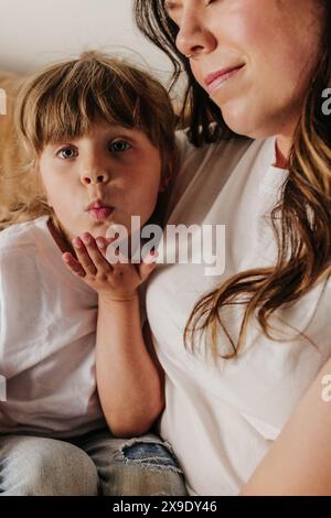 Ein junges Mädchen bläst Küsse, während es mit Mom auf der Couch kuschelt Stockfoto