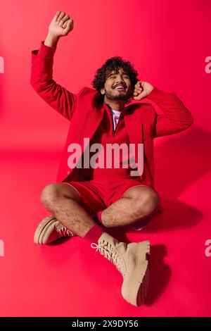 Ein stilvoller junger Mann in einem leuchtend roten Anzug sitzt nachdenklich auf dem Boden. Stockfoto