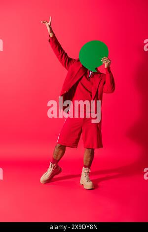 Hübscher junger Indianer in einem leuchtenden roten Anzug, der spielerisch eine grüne Sprechblase hält. Stockfoto