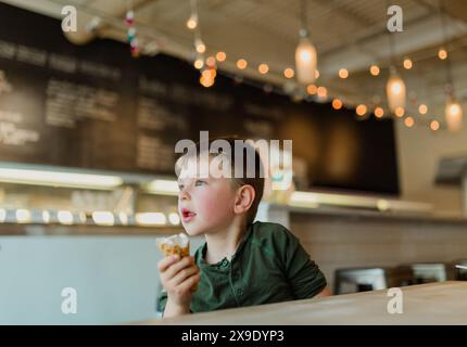 Kleiner Junge, der in einer gemütlichen Eisdiele einen Eisbecher genießt Stockfoto