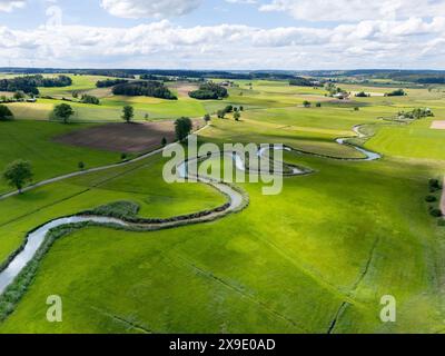 Drohnenaufnahme eines weiten europäischen Tals, in dem sich ein kleiner Bach durch grüne Wiesen und Felder schlängelt. Stockfoto
