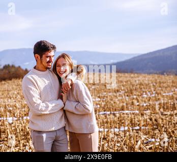 Fröhliches Paar, das sich auf einem ausgeernteten Feld mit malerischen Bergen umgibt Stockfoto