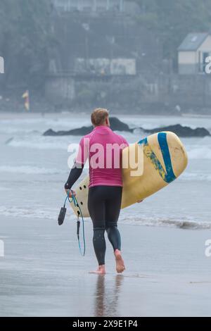 Ein männlicher Surfer mit seinem Surboard, der am GT Western Beach in Newquay in Cornwall in Großbritannien entlang spaziert Stockfoto