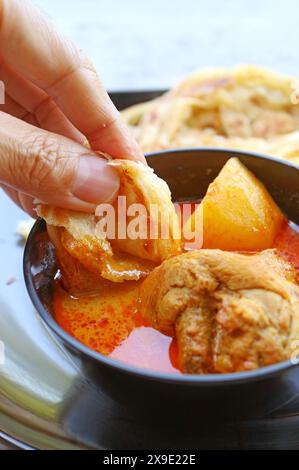 Von Hand eingetauchtes Roti-Fladenbrot in scharfe indische Hühnchen-Curry-Suppe Stockfoto