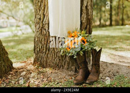 Brautstrauß mit Sonnenblumen sitzt in Cowgirl-Stiefeln von Kleid Stockfoto