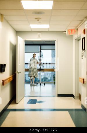 Älterer Krebspatient, der ein Kleid trägt, schaut aus dem Fenster des Krankenhauses Stockfoto