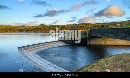 Wasser stürzt Stufen vom ruhigen malerischen künstlichen See herunter, unter einer Steinbrücke (sonniger Abend, blauer Himmel und weiße Wolken) - Swinsty Reservoir, England Großbritannien. Stockfoto