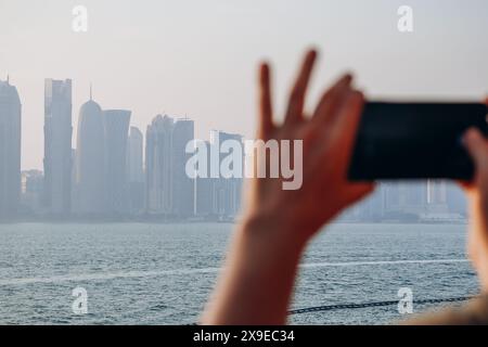 Ein Mann macht ein Telefonfoto der Skyline von Doha, West Bay. Der Vordergrund ist absichtlich unscharf. Stockfoto