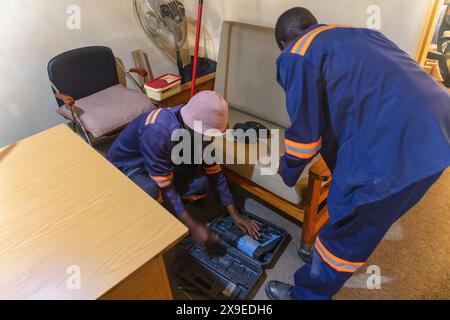 Zwei afrikanische Arbeiter mit einer Bohrmaschine, die das Internet in einem Raum repariert Stockfoto