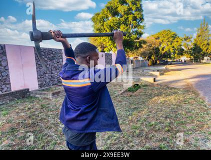 afrikanischer Arbeiter mit einer Spitzhacke, der den Boden auf der Straße gräbt Stockfoto