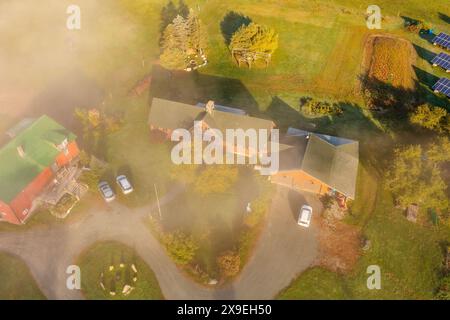 Bauernhof mit Nebengebäuden im Herbstwald unter den Wolken. Draufsicht der Drohne. New Hampshire, USA Stockfoto