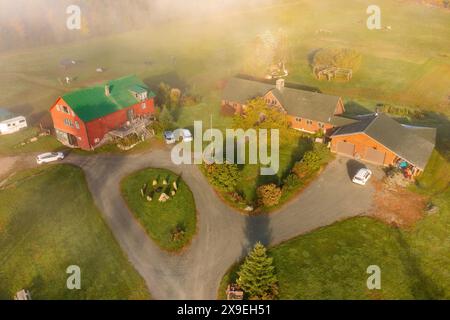 Bauernhof mit Nebengebäuden im Herbstwald unter den Wolken. Draufsicht der Drohne. New Hampshire, USA Stockfoto