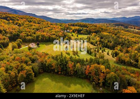 Der Herbstwald schmückt ein abgelegenes Bauernhaus unter Wolken und Bergkulisse. Dron-Ansicht. Vermont, USA Stockfoto