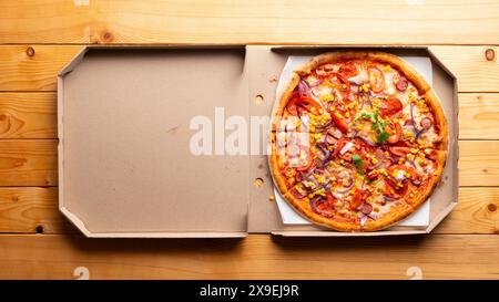 Peperoni-Pizza mit Paprika, Zuckermais und Rucola in offener Schachtel auf natürlichem Holzküchentisch, flacher Lay View mit Kopierraum Stockfoto