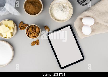 Digitales Touchscreen-Tablet mit Zutaten für Brownie-Rezepte und Küchenutensilien auf grauem Hintergrund, Draufsicht. Stockfoto