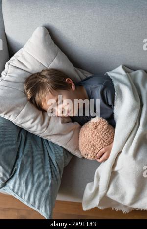 Der Vorschuljunge schläft auf dem Sofa im Wohnzimmer und umarmt seinen Teddybär. Stockfoto