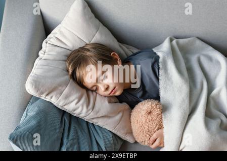 Der Vorschuljunge schläft auf dem Sofa im Wohnzimmer und umarmt seinen Teddybär. Stockfoto