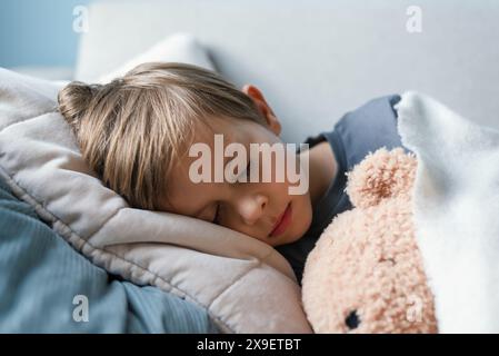 Der Vorschuljunge schläft auf dem Sofa im Wohnzimmer und umarmt seinen Teddybär. Stockfoto