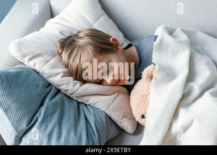 Der Vorschuljunge schläft auf dem Sofa im Wohnzimmer und umarmt seinen Teddybär. Stockfoto