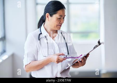 Asiatische Ärztin, die Patientenakte in der Arztpraxis überprüft Stockfoto