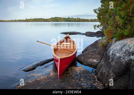 Rotes Holzkanu am felsigen Ufer eines Boundary Waters Sees im Morgenlicht im Herbst Stockfoto