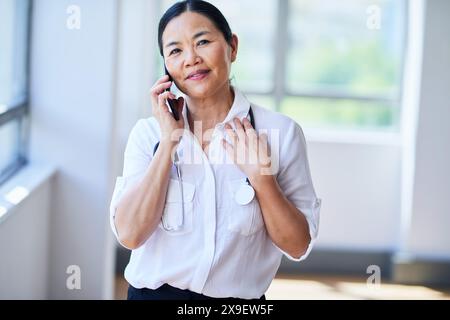Selbstbewusste Ärztin, die in einem modernen Krankenhaus telefoniert Stockfoto