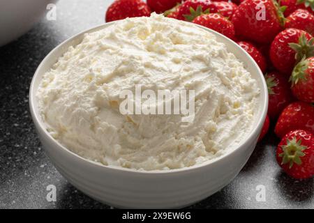 Weiße Schüssel mit italienischem Mascarpone in Nahaufnahme und frischen Erdbeeren im Hintergrund Stockfoto