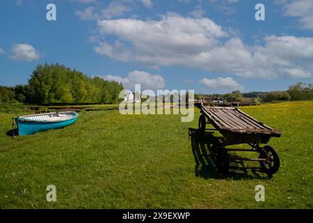 Die Wasserwiesen am Fluss Stour in Sudbury, Suffolk, Großbritannien mit einem offenen Holzboot, einem alten Holzwagen und der alten Wassermühle Stockfoto